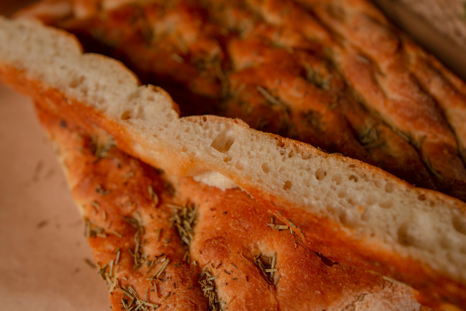 Golden rosemary focaccia cut into slices, glossy with olive oil